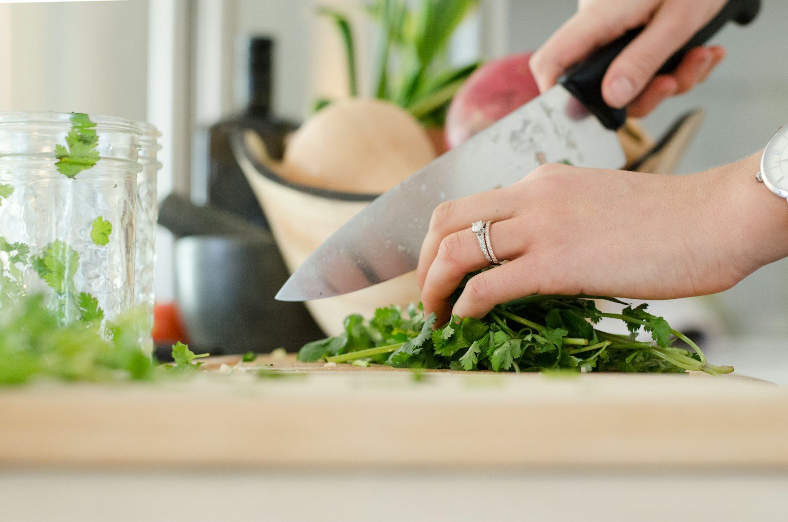 Hands chopping fresh herbs on a wooden board in a light kitchen